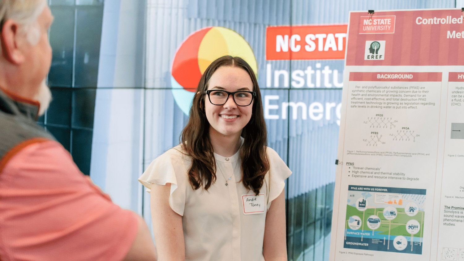Image shows a young woman wearing glasses standing next to a poster board.