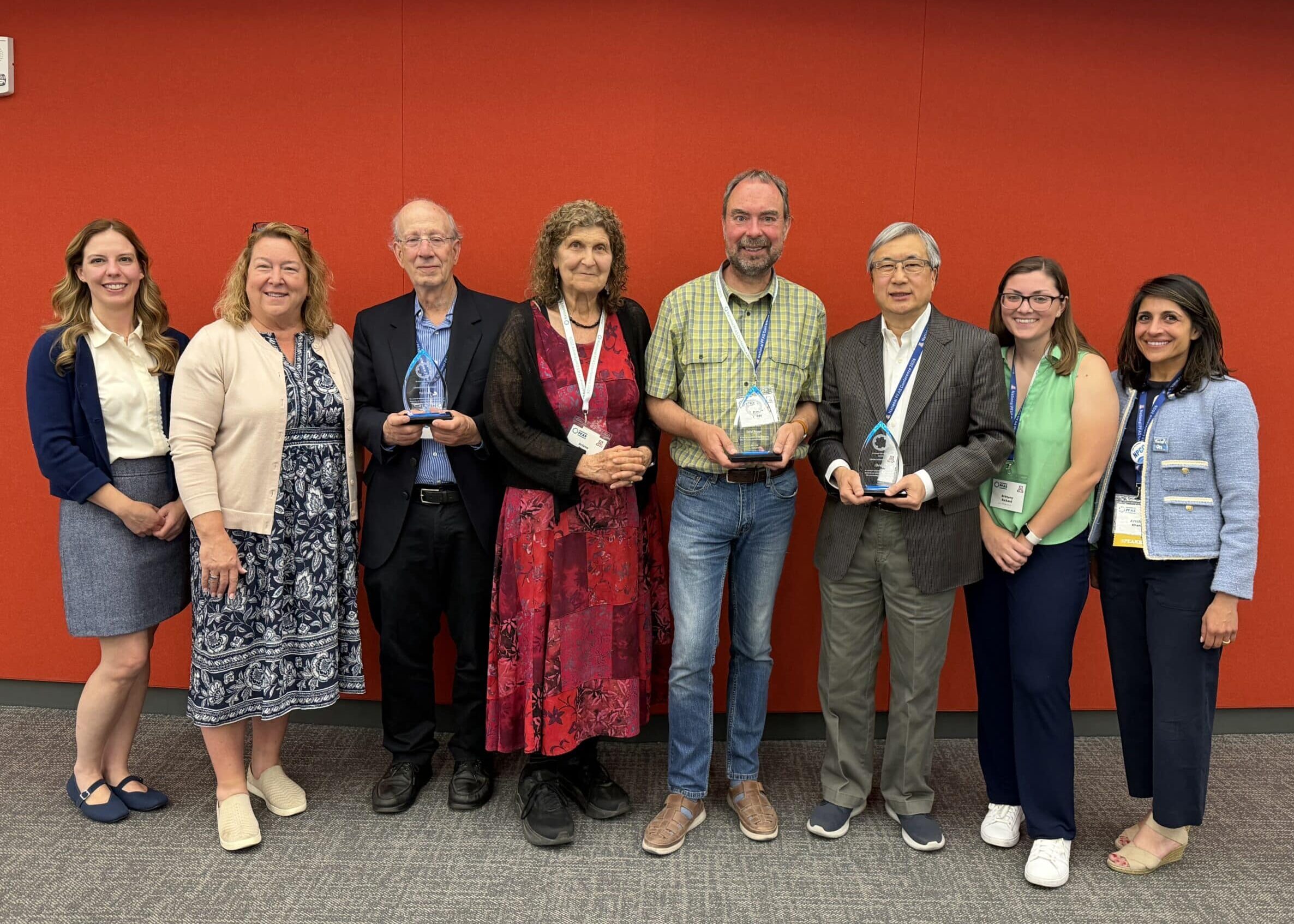 A group of professionally dressed people holding awards in front of a red wall.